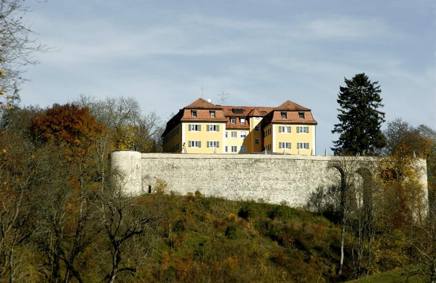 Blick auf das Schloss Grafeneck aus Richtung Marbach kommend. Zu sehen ist das gelbe Renaissance-Schloss auf einer Anhöhe. Unterhalb des Schlosses befindet sich die graue Schlossmauer.