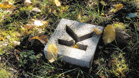 Ein quadratischer Betonstein in einer Wiese. In den Stein ist der Buchstabe K eingraviert.